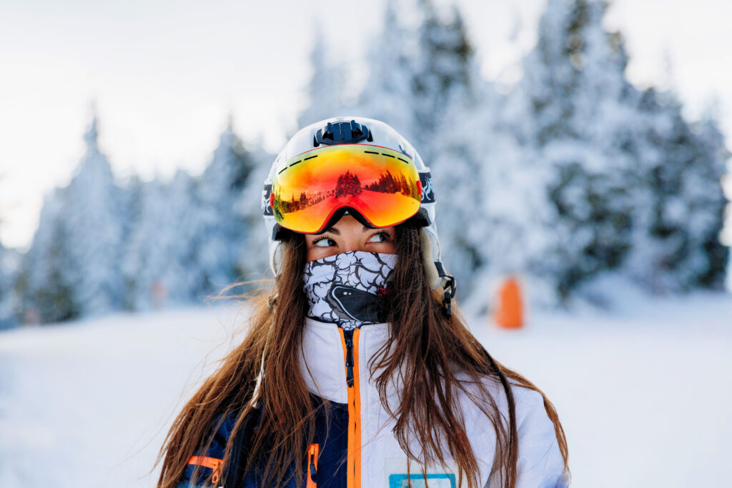 woman-owned ski company stroytelling video production with a brunette ski woman looking to the side with goggles on her head and helmet with snowy trees behind her