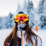 woman-owned ski company stroytelling video production with a brunette ski woman looking to the side with goggles on her head and helmet with snowy trees behind her